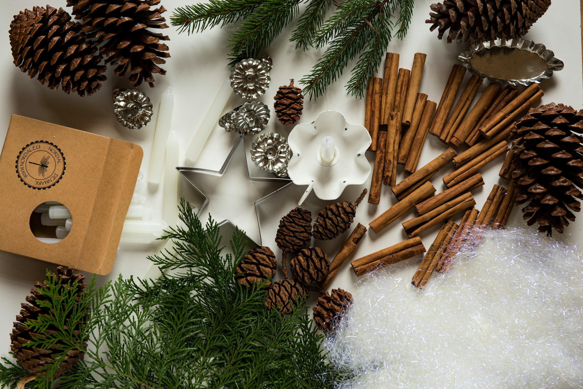Festive craft materials with candles, pine cones, cinnamon sticks, and evergreen branches